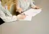 woman signing on white printer paper beside woman about to touch the documents