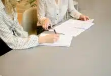 woman signing on white printer paper beside woman about to touch the documents