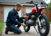 Comment entretenir une moto 50cc 4 temps homologuée pour la garder en parfait état ? Jeune homme vérifiant la chaîne d'une moto propre en extérieur